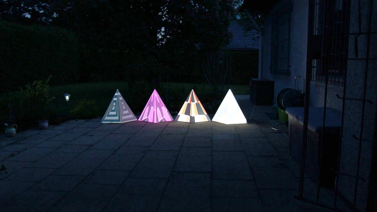 Tetrahedrons with colorful visuals projected on them in the garden.